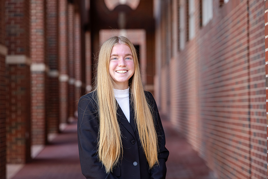 girl with a black blazer and white dress shirt stands in front of a brick building