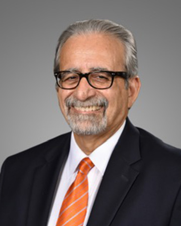 A professional headshot of a man in a black suit with orange tie.