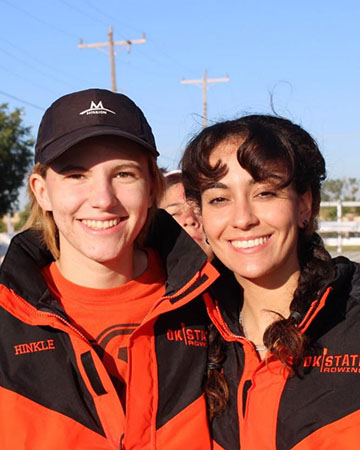 Two students in bright orange and black jackets that have OSU Row on them.