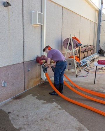A person connecting a fire hose to a spout outside of a fire laboratory.