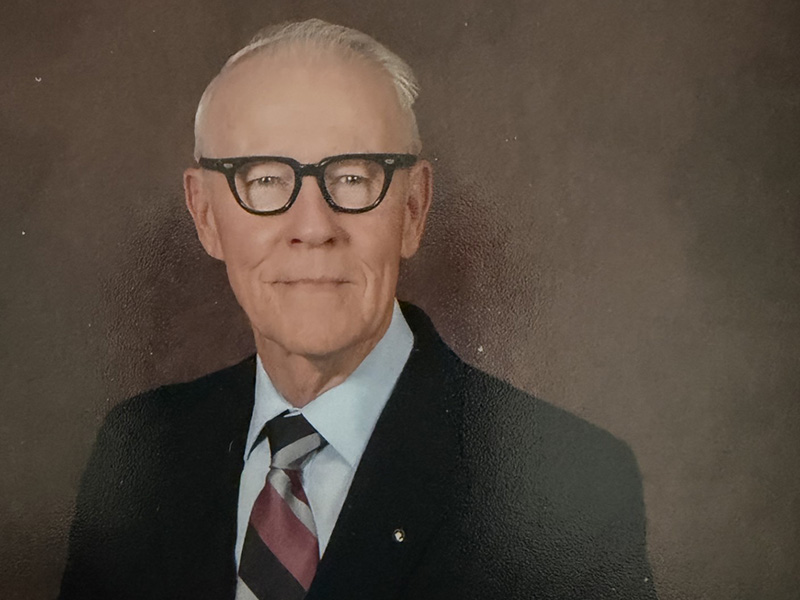 Man with glasses wearing a black suit and tie.