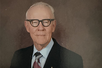Man with glasses in a black suit and tie