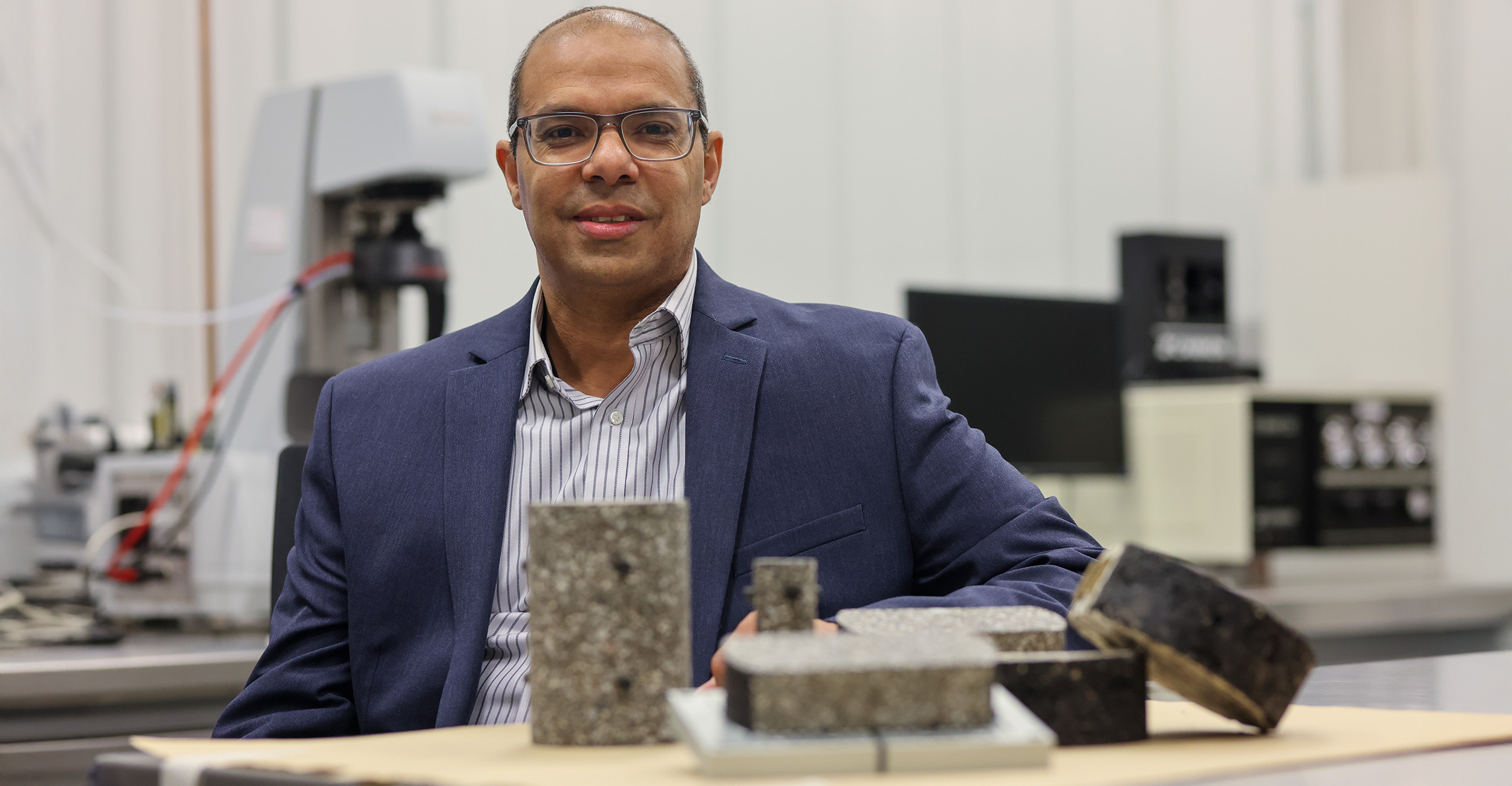 Researcher seated behind several concrete or composite material samples displayed on a laboratory table.