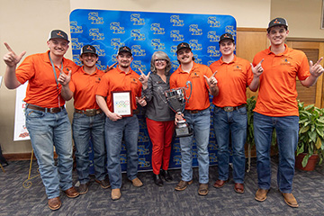 A group of Oklahoma State University students and a faculty member pose together holding a gold medal plaque and trophy, celebrating a first‑place team win in a fire protection or safety engineering competition.