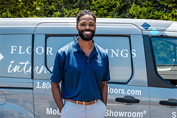 Person wearing a blue polo shirt standing in front of a company van with flooring business branding.