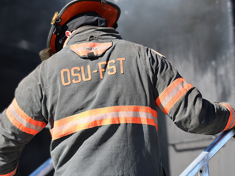The back of a fire fighter with OSU-FST printed on the back of his fire jacket