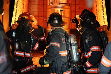 Three fire fighters stand facing a fire in the fire simulator