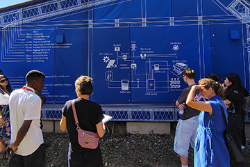 A large outdoor blue architectural mural displays white technical drawings and labels for an energy-efficient building system.