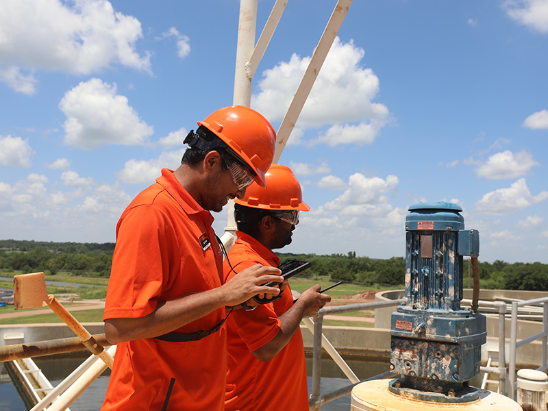Two men in orange polos use equipement to assess energy usage.