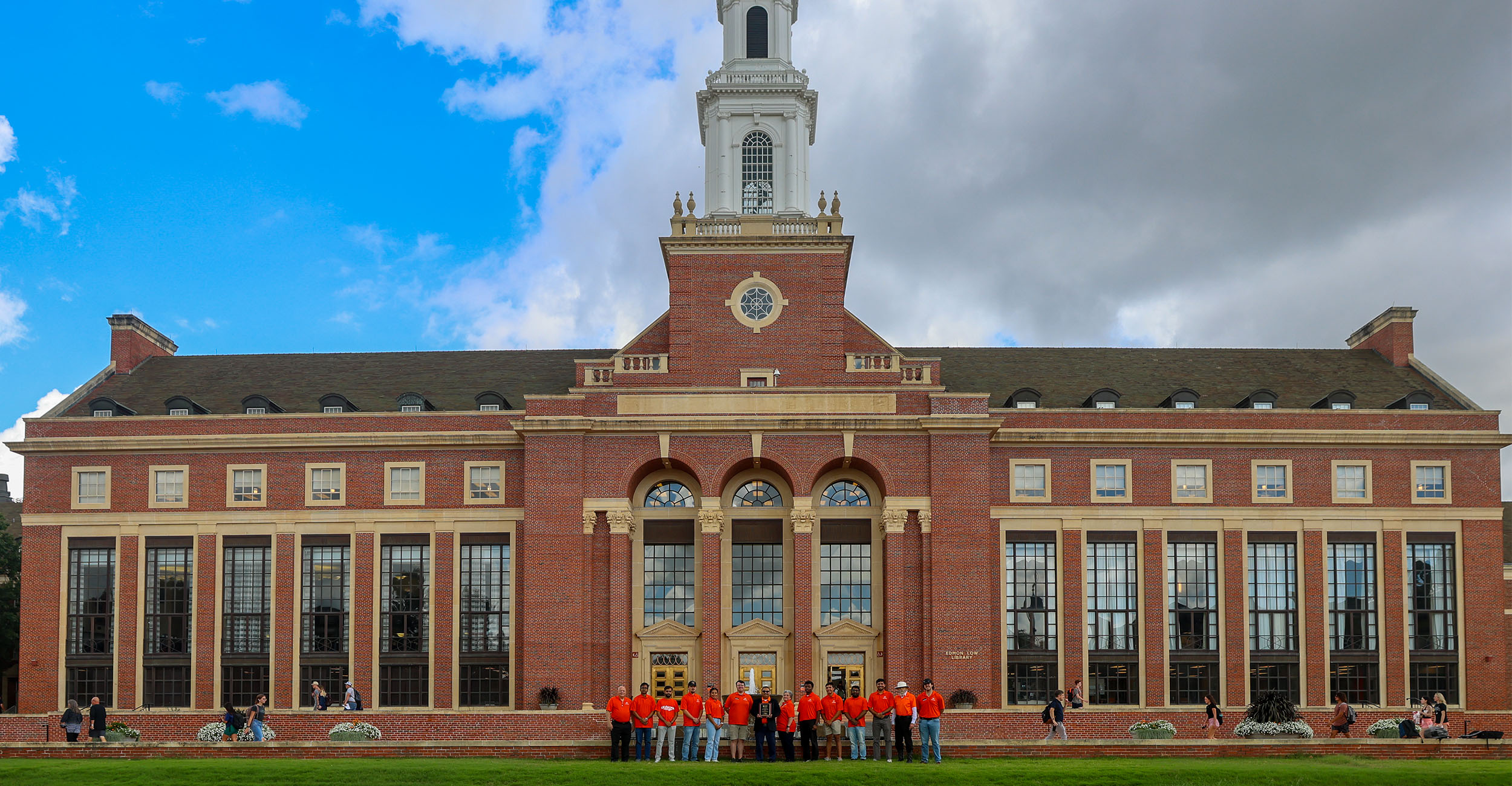 A group of people in orange polos pose in front of Edmon Low Library.
