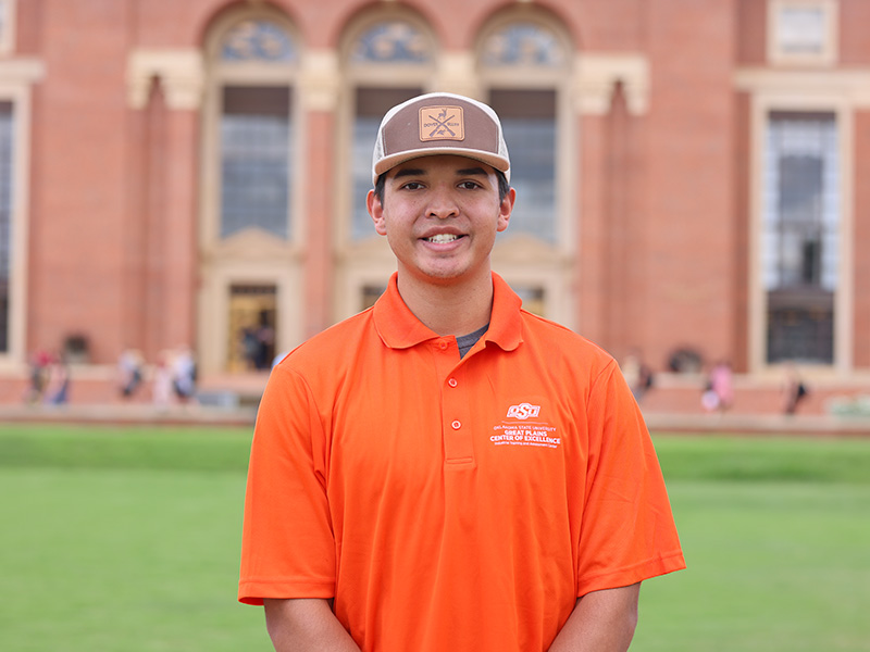 A young man in an orange polo poses on the lawn of Edmon Low library.