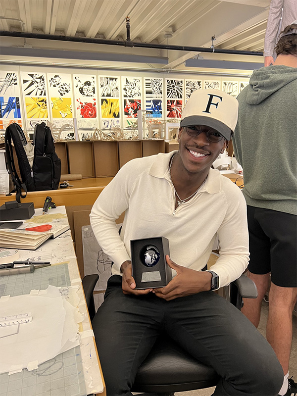 Jai Simpson sits in a chair while holding an award for work he has done as an architecture student at Oklahoma State University.
