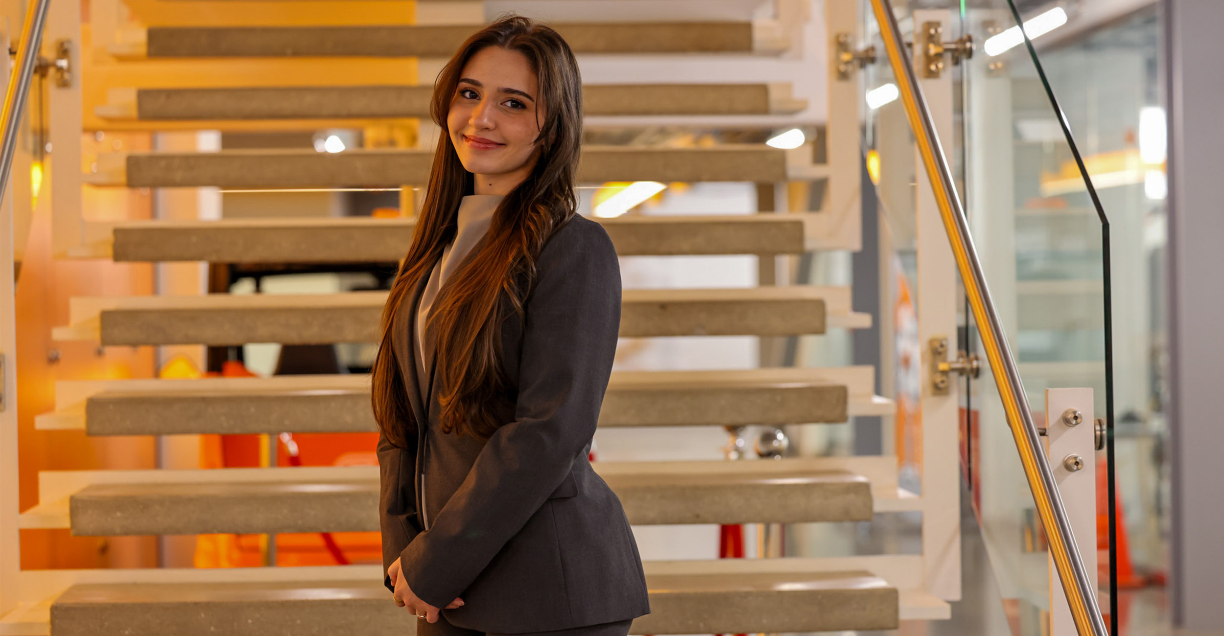 A woman stands on a staircase wearing a pantsuit in a well-lit location.
