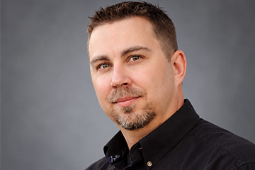 Professional portrait of a man with short hair and a black button up shirt
