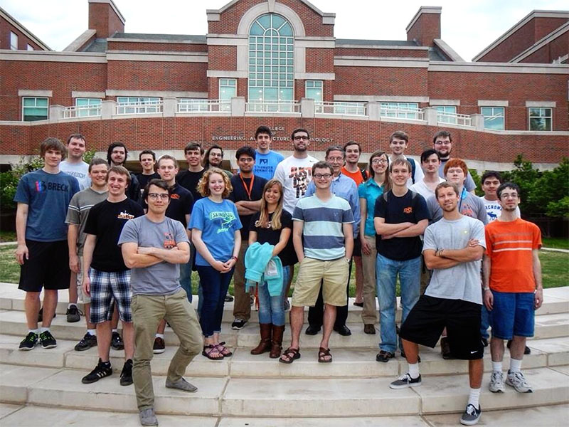 Group of students standing on steps in front of a large brick engineering building on a college campus.