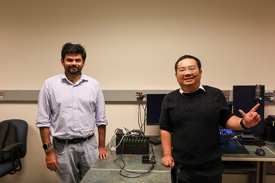 A photograph of two men standing in a computer laboratory beside a workbench covered with electronic equipment