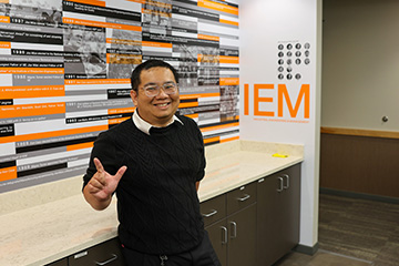A color photograph shows a smiling person standing in an industrial engineering department lobby.