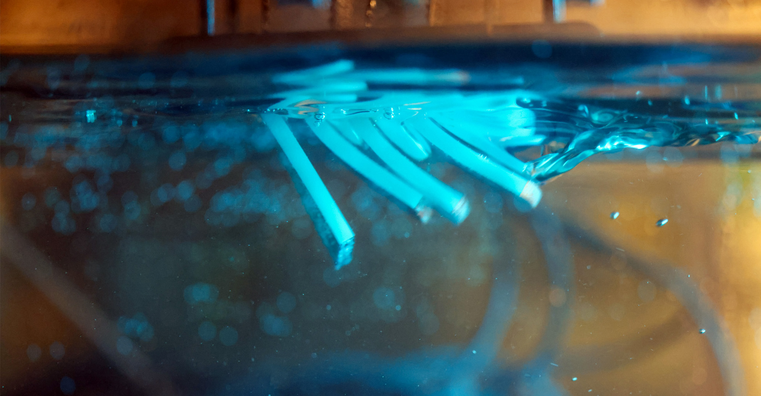 A close-up underwater view shows a series of flexible, paddle-like blue elements moving in sequence beneath the water’s surface, demonstrating a bio‑inspired robotic motion pattern designed to study fluid movement and propulsion.