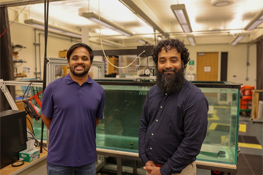 Two researchers stand in a laboratory beside a large water tank and experimental equipment, illustrating an aquatic or bio‑inspired robotics research environment.
