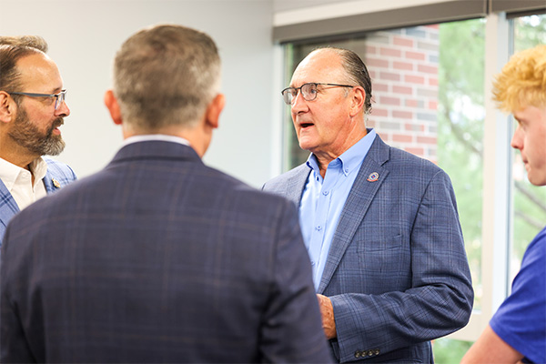 An indoor photograph shows four men engaged in conversation. 