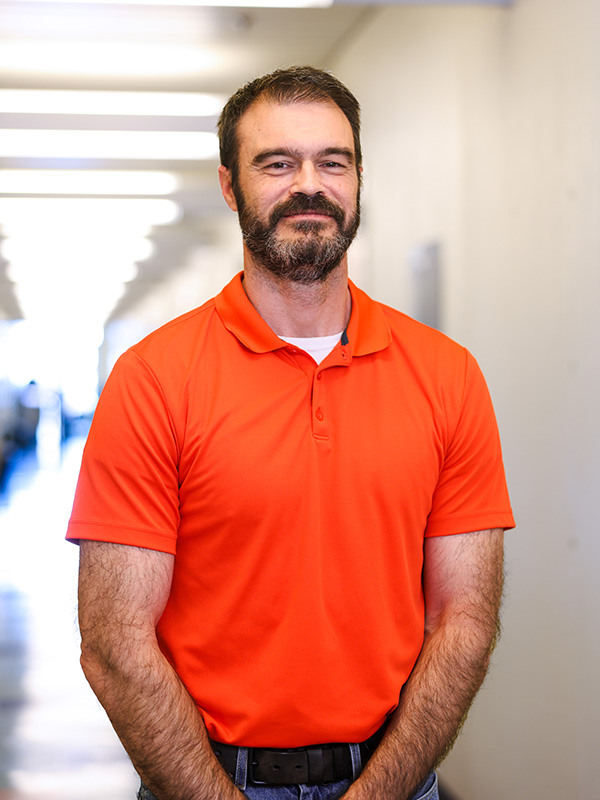 A man in a bright orange polo shirt standing in a well-lit hallway.