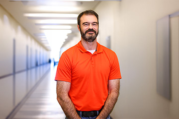 A man in a bright orange polo shirt standing in a well-lit hallway.