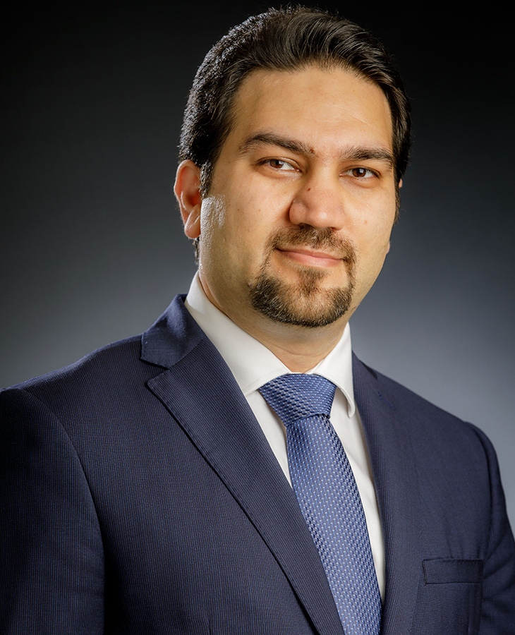 A professional headshot of a man in a navy blue suit.