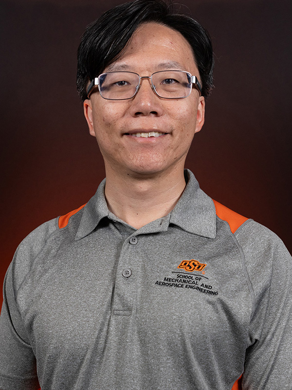 Professional headshot of a faculty member wearing glasses and a gray Oklahoma State University School of Mechanical and Aerospace Engineering polo shirt against a dark background.