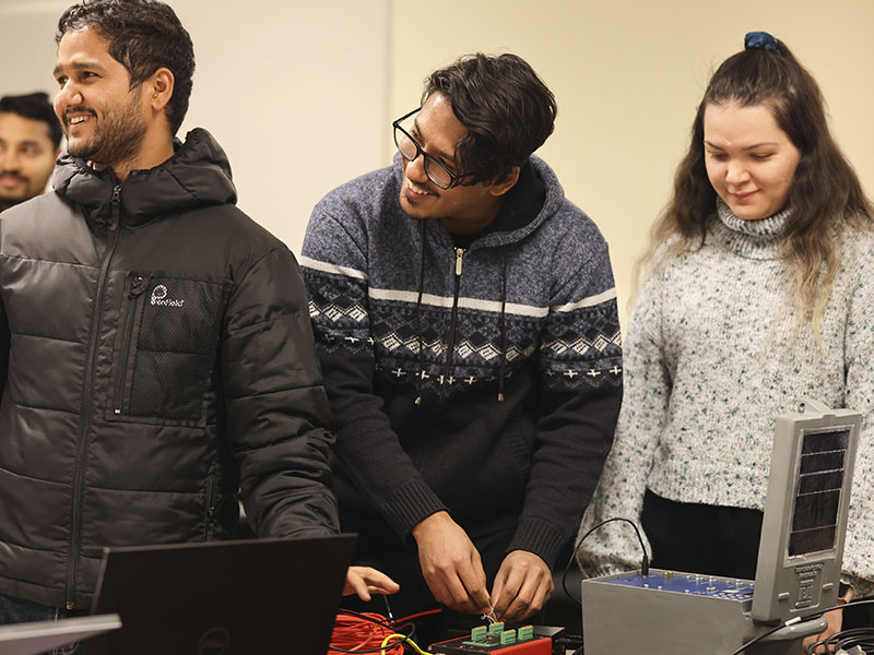 Students work with electronic testing equipment and sensors in a laboratory setting during a transportation engineering research project.