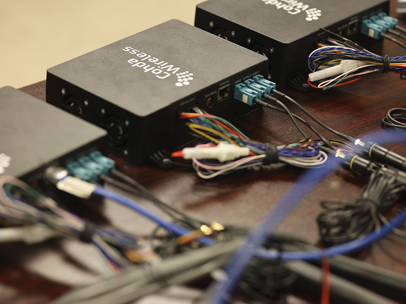 Several wireless communication devices connected by cables and wiring are arranged on a laboratory table as part of a research system.