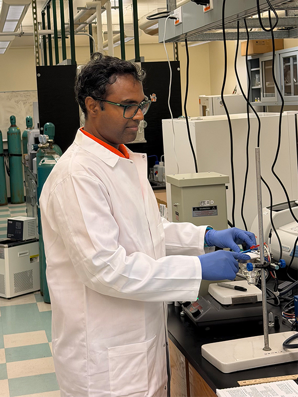 Image of Dr. Praveen Meduri wearing blue gloves and a white lab coat using a piece of piece of lab equipment