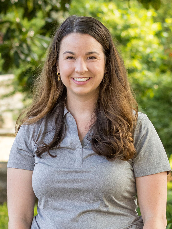 Outdoor portrait of a person wearing a light gray polo shirt, standing in front of a blurred green garden setting.