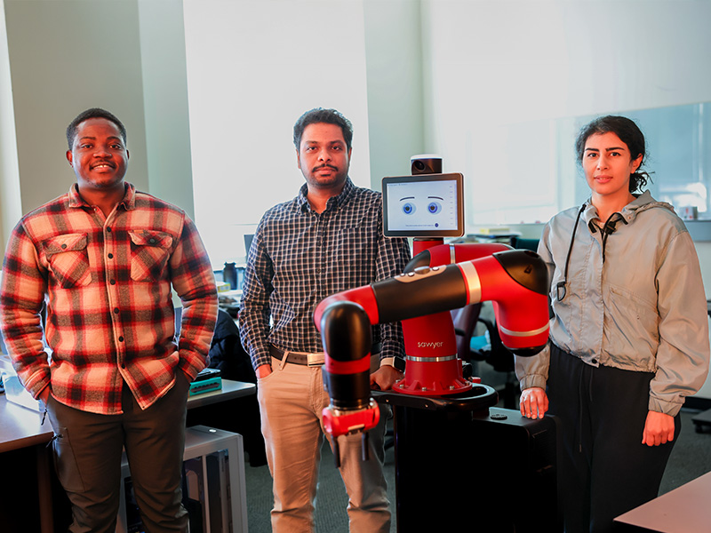 A group of three researchers posing with a red robot for a photo.