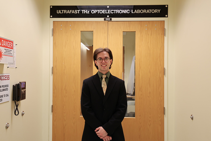 An individual stands centered in front of closed wooden doors labeled “Ultrafast THz Optoelectronic Laboratory,” indicating the entrance to a specialized research lab.