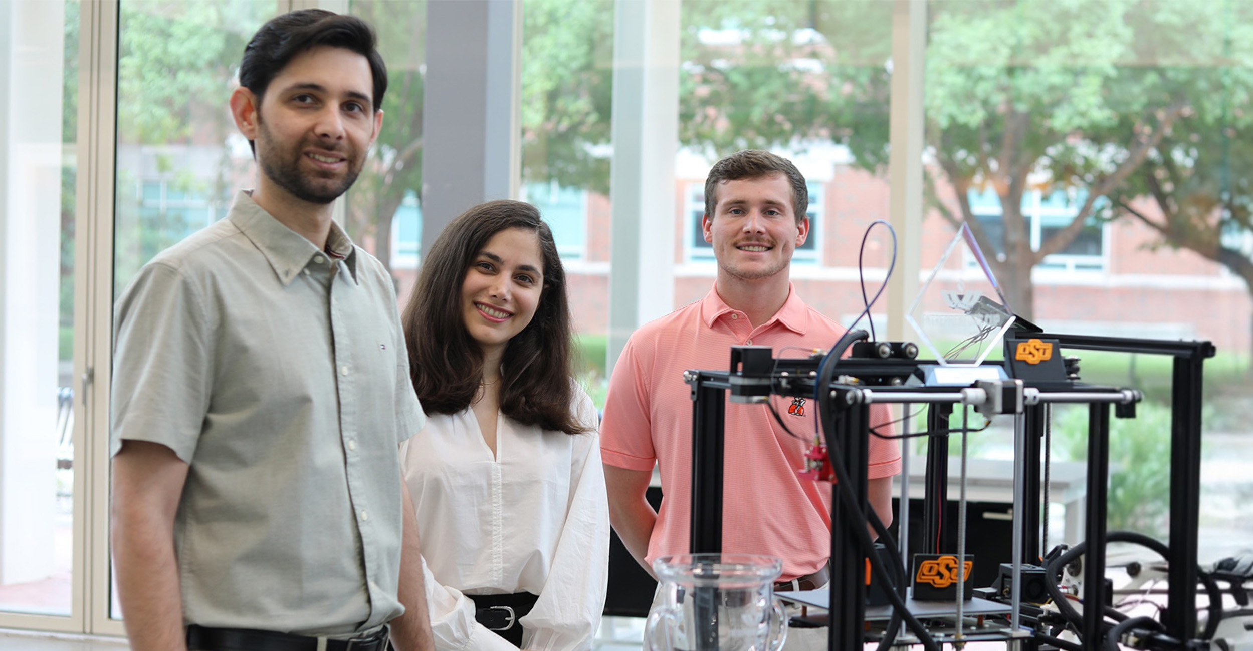 Three Oklahoma State University students stand for a portrait photo with SCIVINCE, a prototype 3D-printer that uses counter-gravity printing. They are pictured in the test arena inside ENDEAVOR Lab at Oklahoma State University.