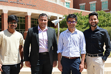 Four men stand side by side outdoors in front of a brick building labeled “College of Engineering, Architecture, Technology
