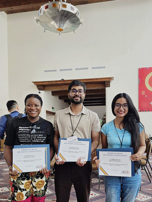Three graduate students stand with paper certificates received during the