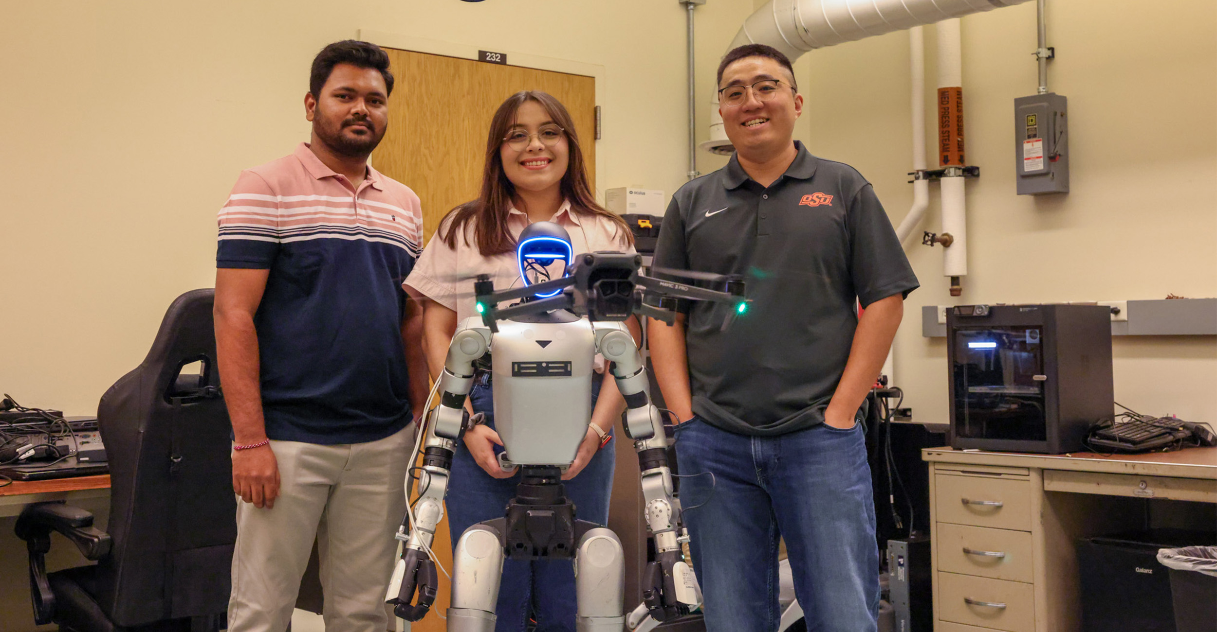 The image features three individuals standing in a laboratory setting alongside a humanoid robot.