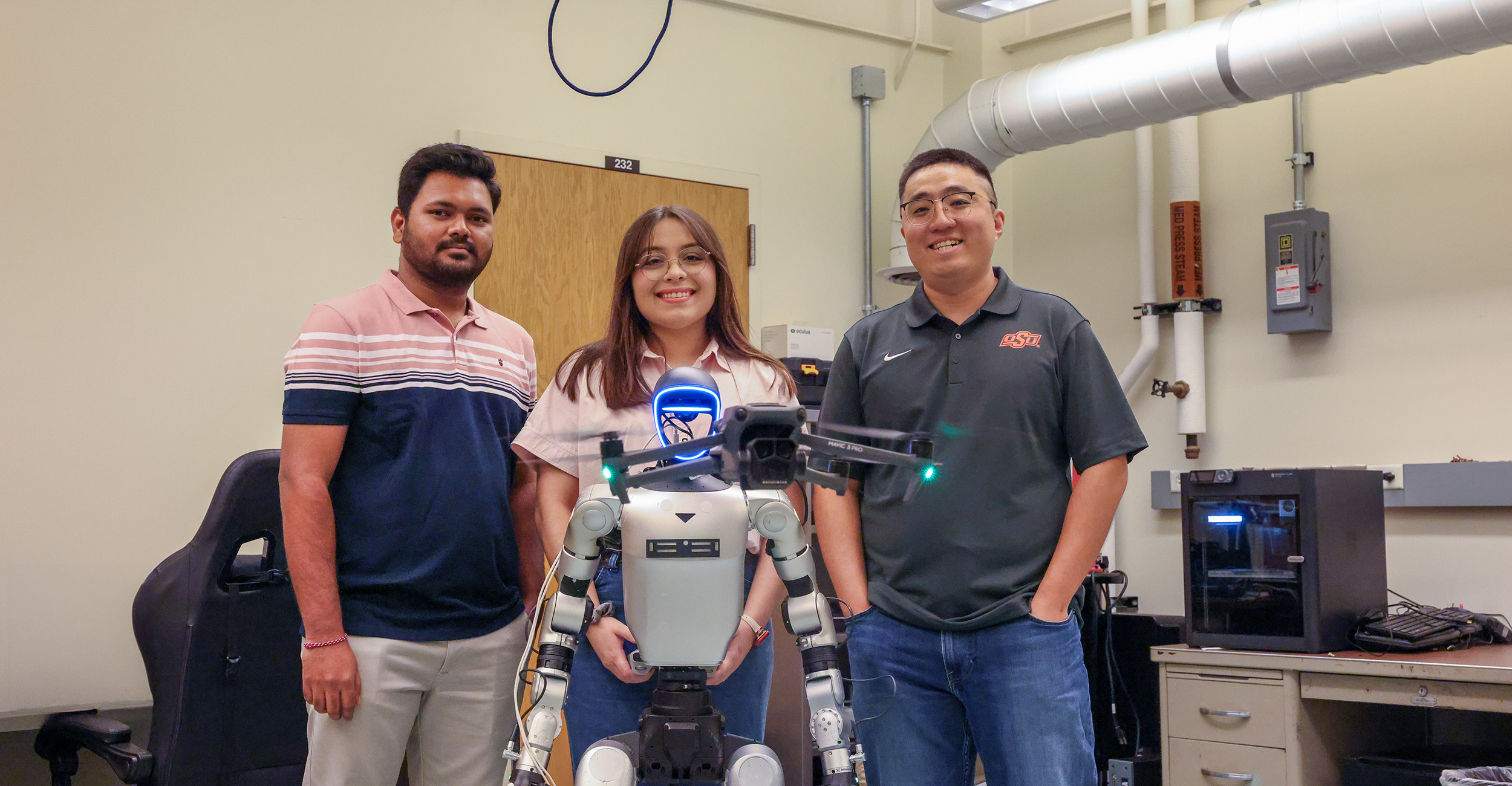 Three researchers pose in a laboratory beside a humanoid robot, with a drone positioned in front of them.