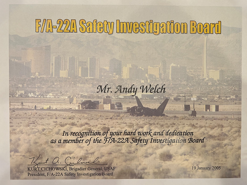 Certificate titled “F/A-22A Safety Investigation Board” awarded to Mr. Andy Welch, featuring a desert scene with a damaged aircraft and a city skyline in the background, dated January 19, 2005.