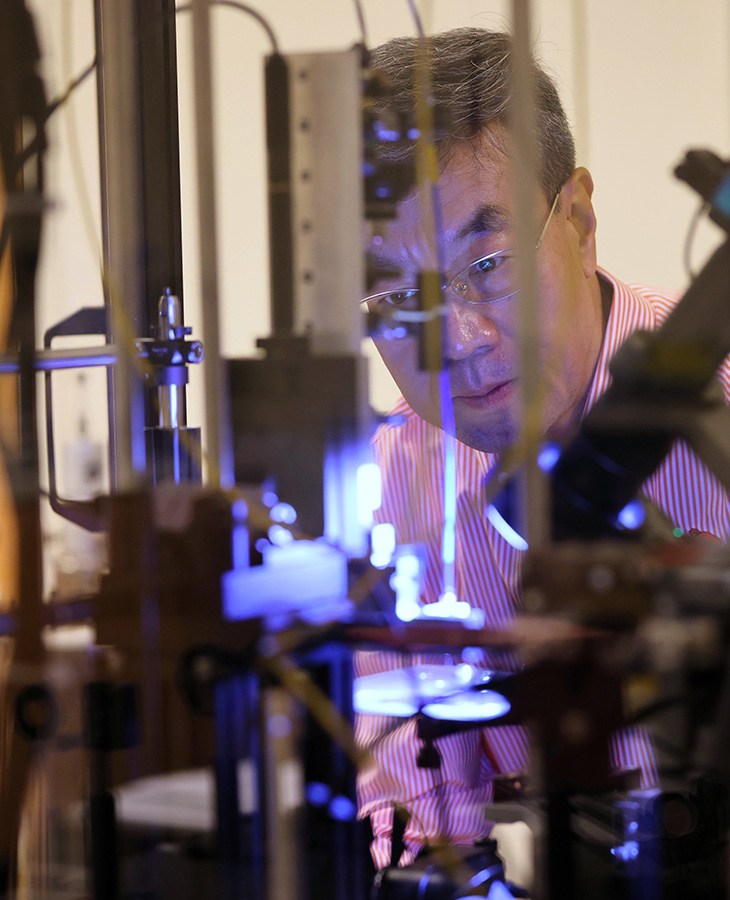 A man stands in a laboratory infront of a piece of equipment that is illuminated with bright light.