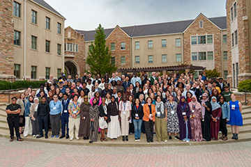 A large group of conference attendees gathers for a group photo in a university courtyard.