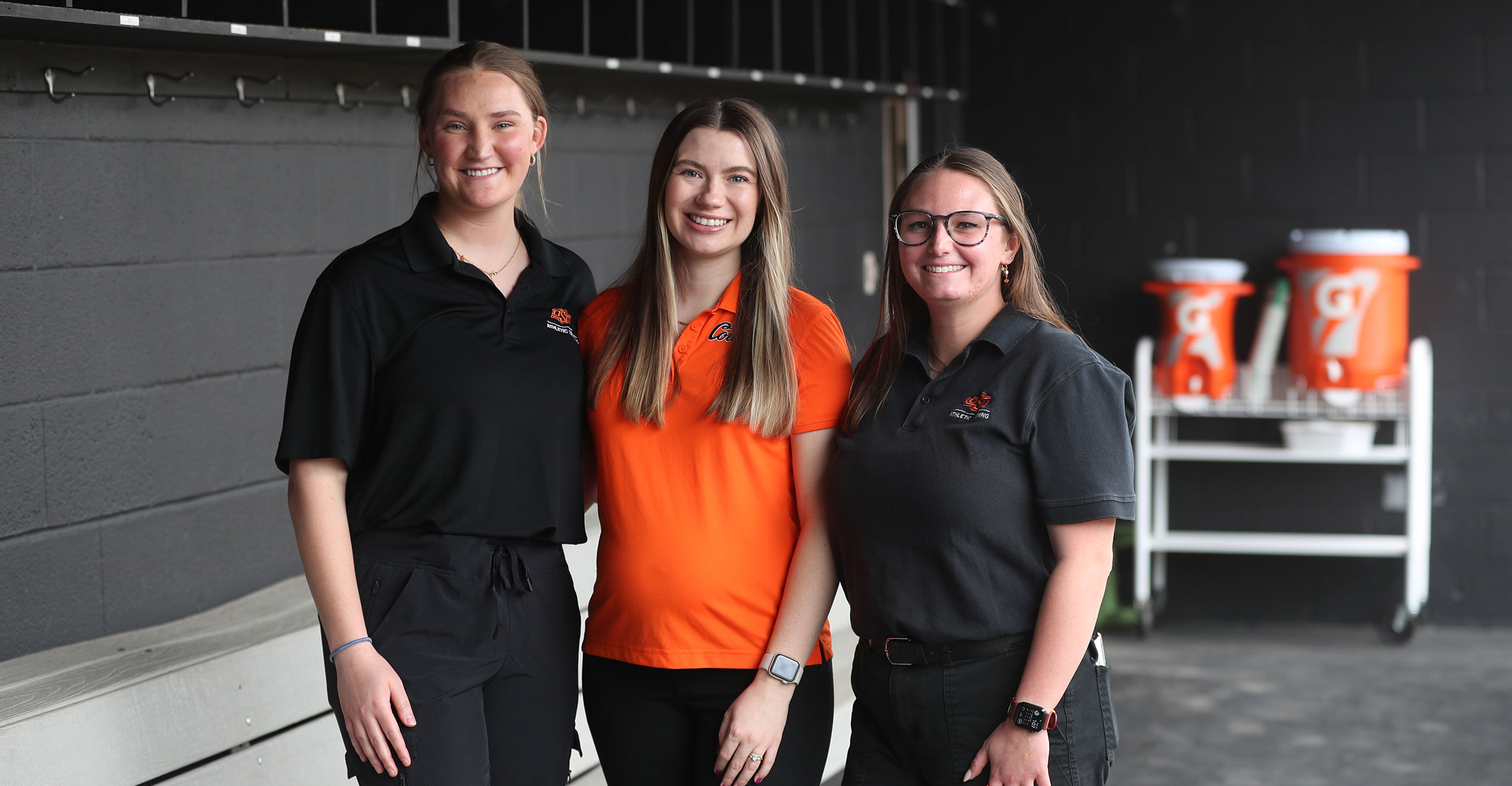 OSU Center for Health Sciences athletic training students Kaleigh Hanzlick (left), Tatum Komlodi and Samantha Renson (right) in the OSU Cowgirl softball dugout.