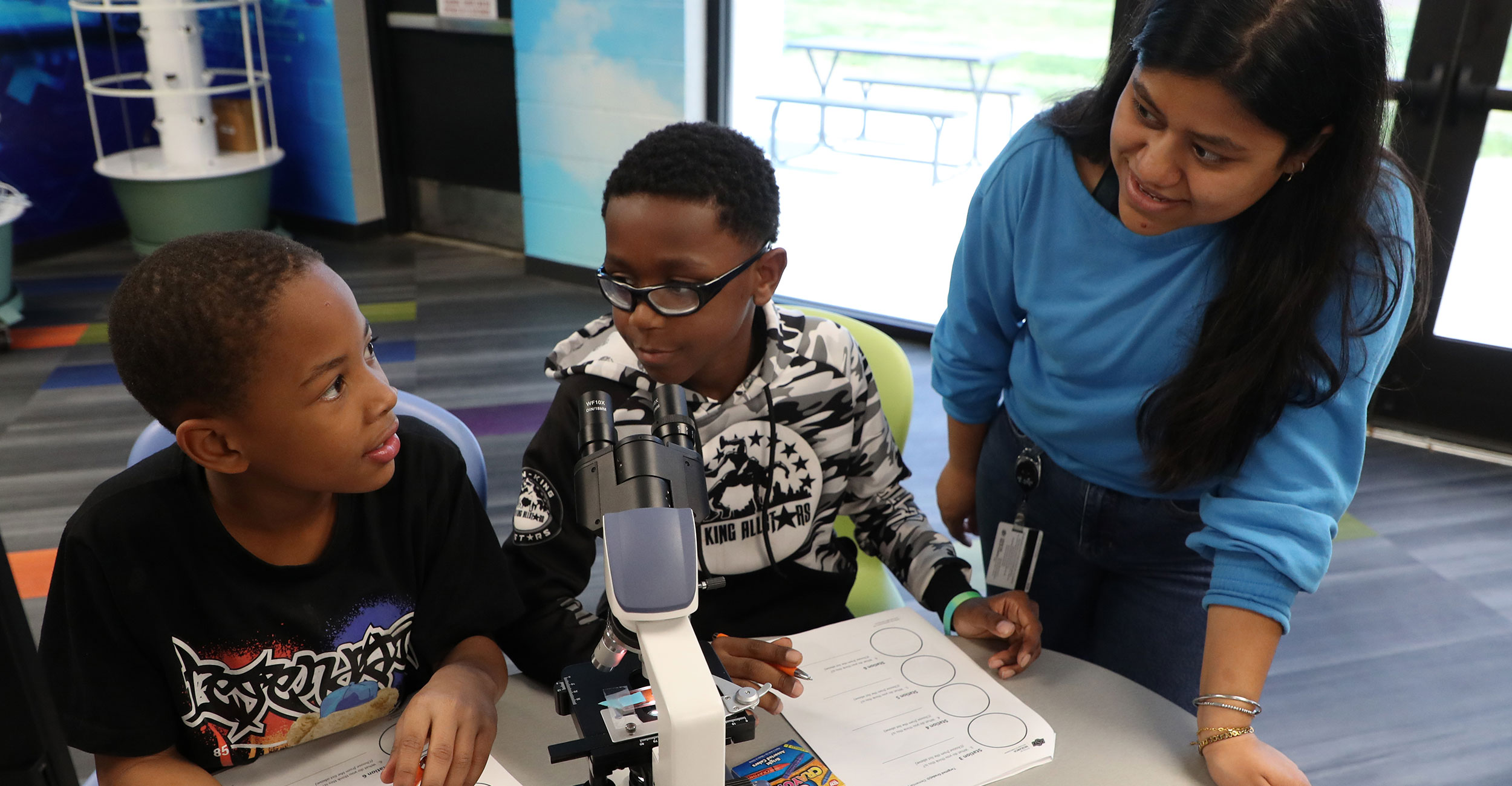 OSU Center for Health Sciences Biomedical Sciences graduate student Frida Miranda (right) helps children use a microscope during a STEM outreach event hosted by the Biomedical Sciences Graduate Student Association at the Salvation Army North Mabee Boys & Girls Club in Tulsa.