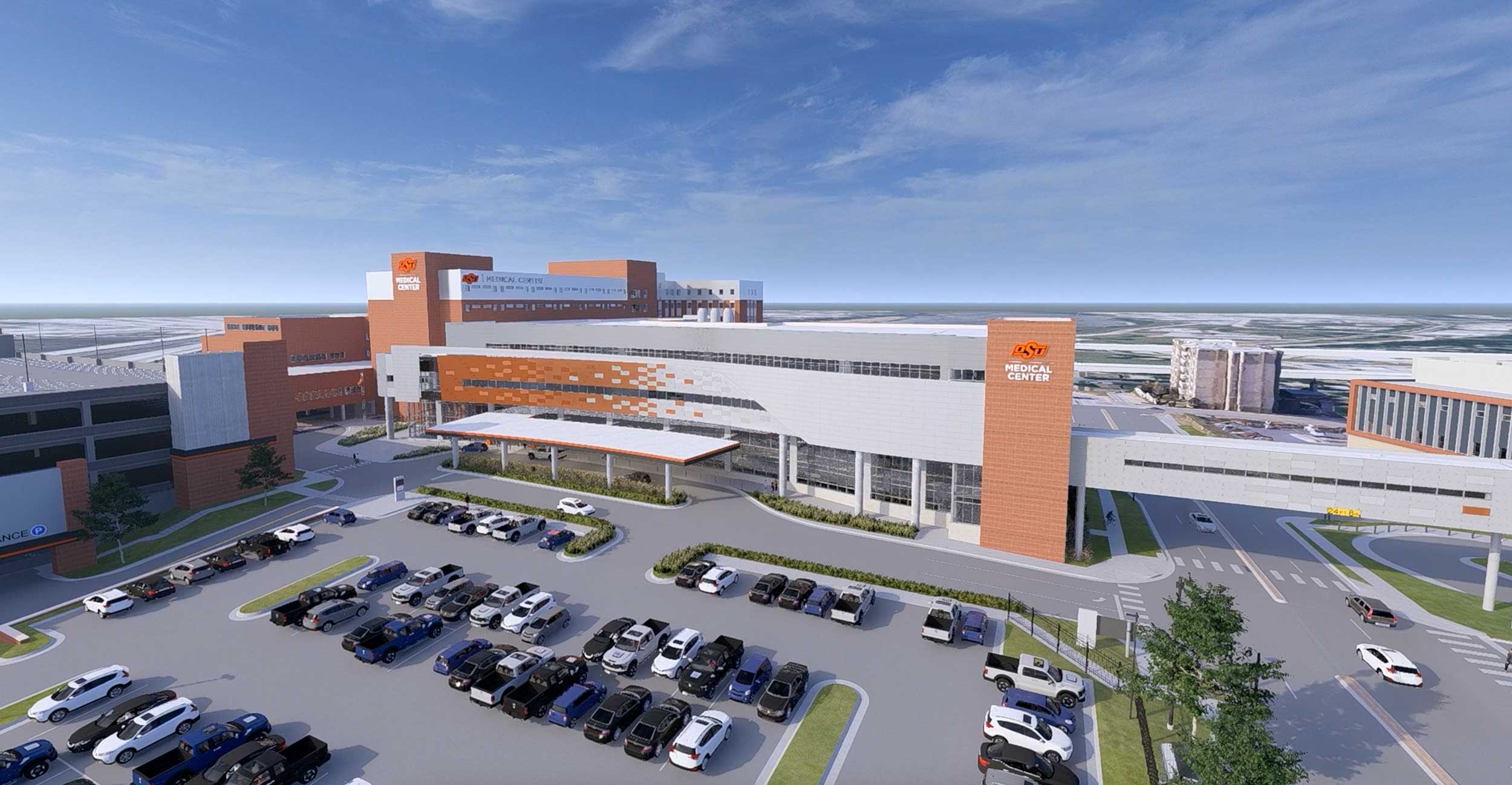 Modern hospital complex with orange and white buildings, large glass windows and a parking lot filled with cars under a clear blue sky.