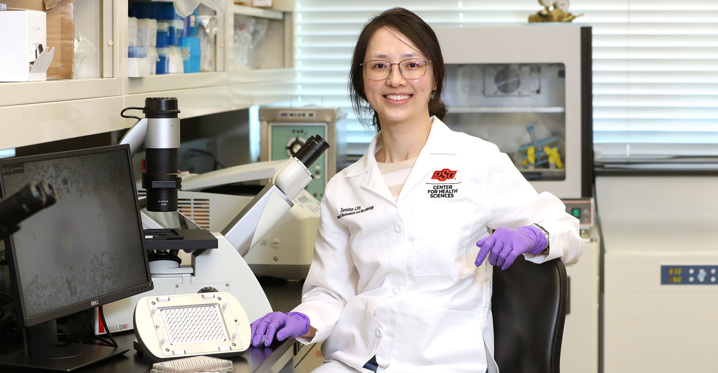 Serene Lim, a fourth-year doctoral student in the Department of Biochemistry and Microbiology at OSU Center for Health Sciences, sits in the lab with the equipment she uses for her research about certain bacteria and its connections to cancer.