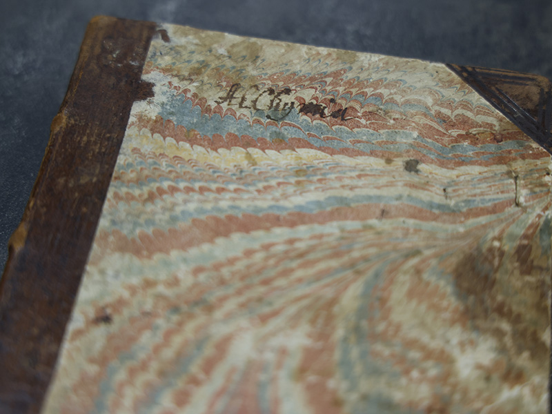 Close-up of an antique book with a marbled paper cover and worn leather binding, highlighting the age and craftsmanship of the historical volume.