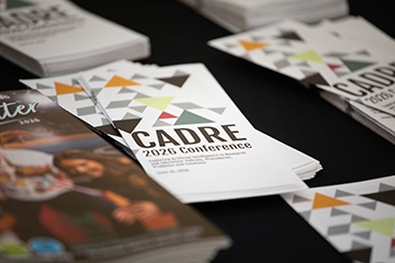 Stacks of printed brochures labeled “CADRE 2026 Conference” with geometric designs are arranged on a table, highlighting promotional materials for an academic event.