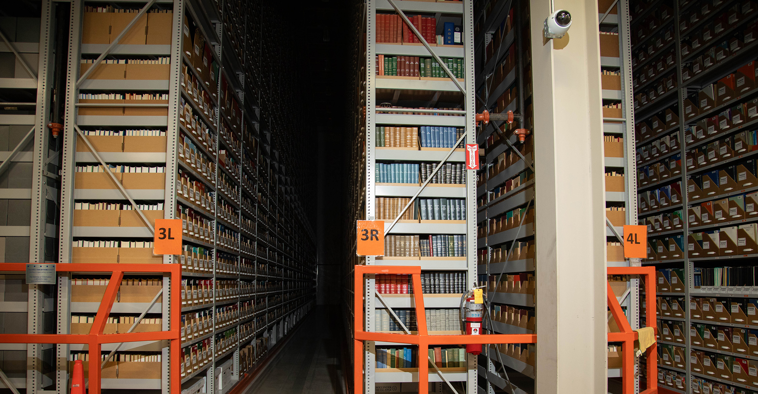 Tall archival library shelving filled with books and labeled storage boxes extends into the distance, illustrating a high-density collection storage area used to preserve and organize library materials.