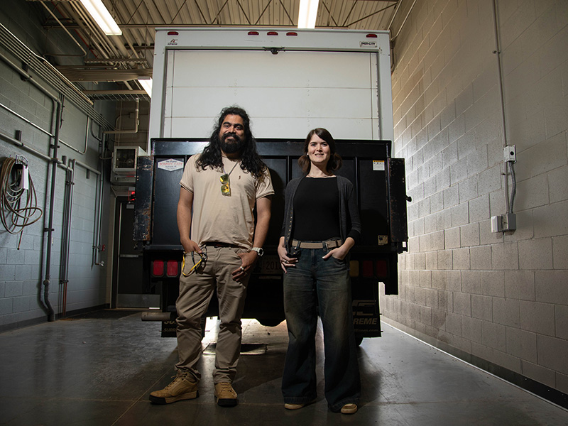 A man and a woman standing at the back of a truck. 